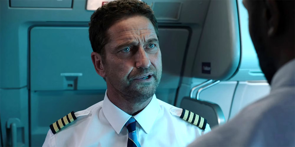 Gerard Butler dressed as a pilot on a plane talking to someone
