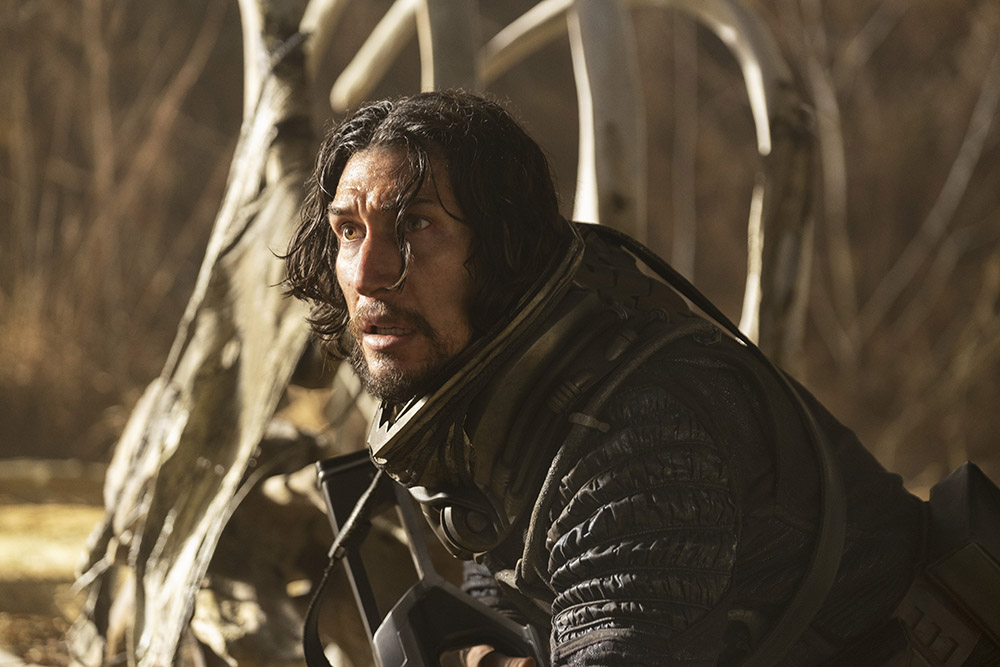 Adam Driver laying on his front, head up starring scared into the distance.