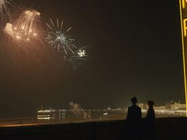 Man and Woman standing on a rooftop at night watching fireworks explode in the sky