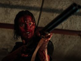 A woman, covered in blood, holding a shotgun