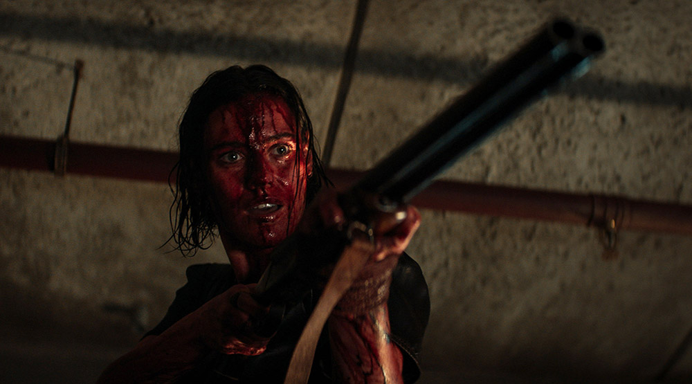 A woman, covered in blood, holding a shotgun