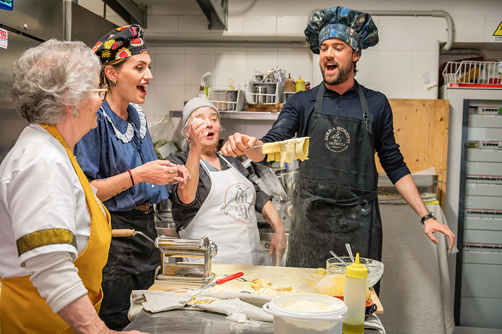Four people making pasta in a kitchen