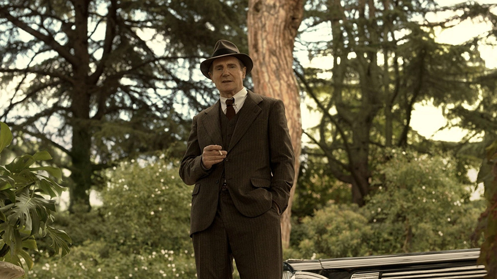 Man in 1930's style suit and hat standing in woods with cigarette in hand