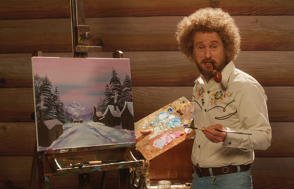 A 70's styled artist holding paintbrush and paints in front of a painted canvas