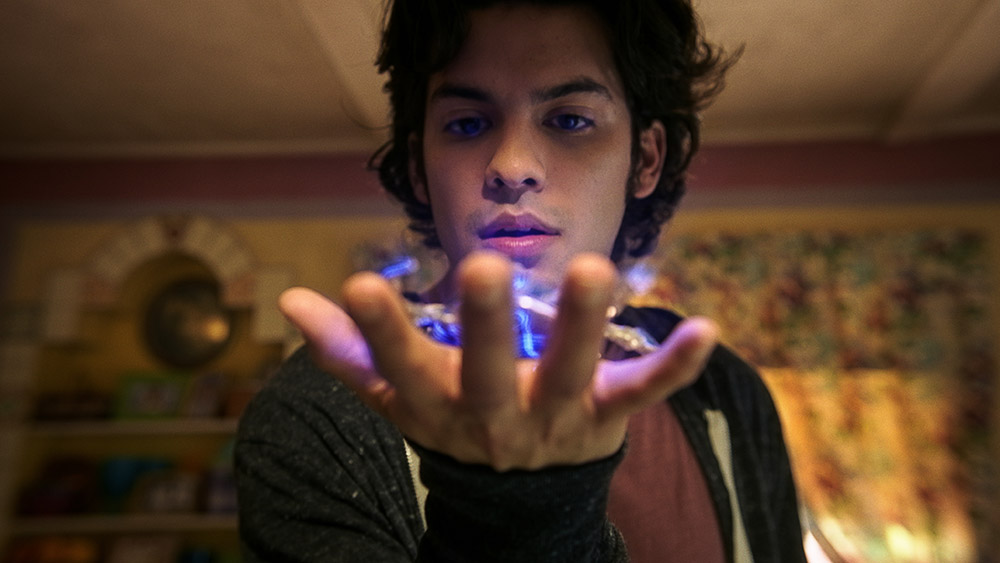 Close up of Teenage Boy holding a glowing blue object in hand in front of his face