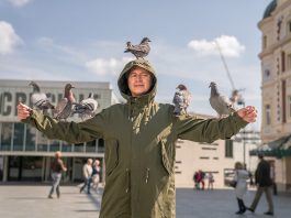 Man standing in t-shape with pigeons on him