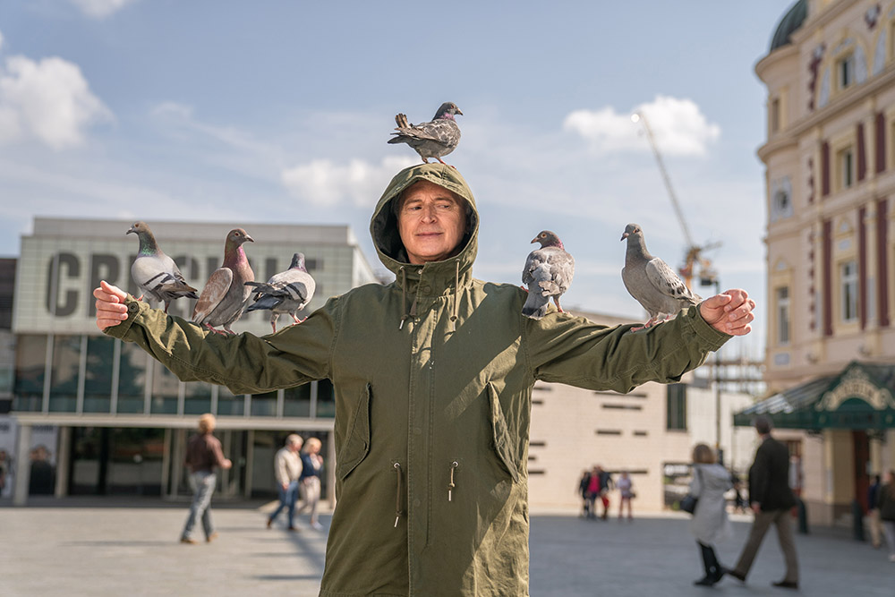 Man standing in t-shape with pigeons on him