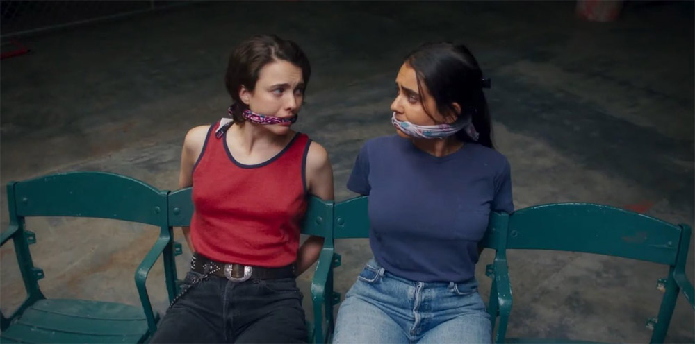 Two young girls tied up to chairs with gags in mouths looking at each other