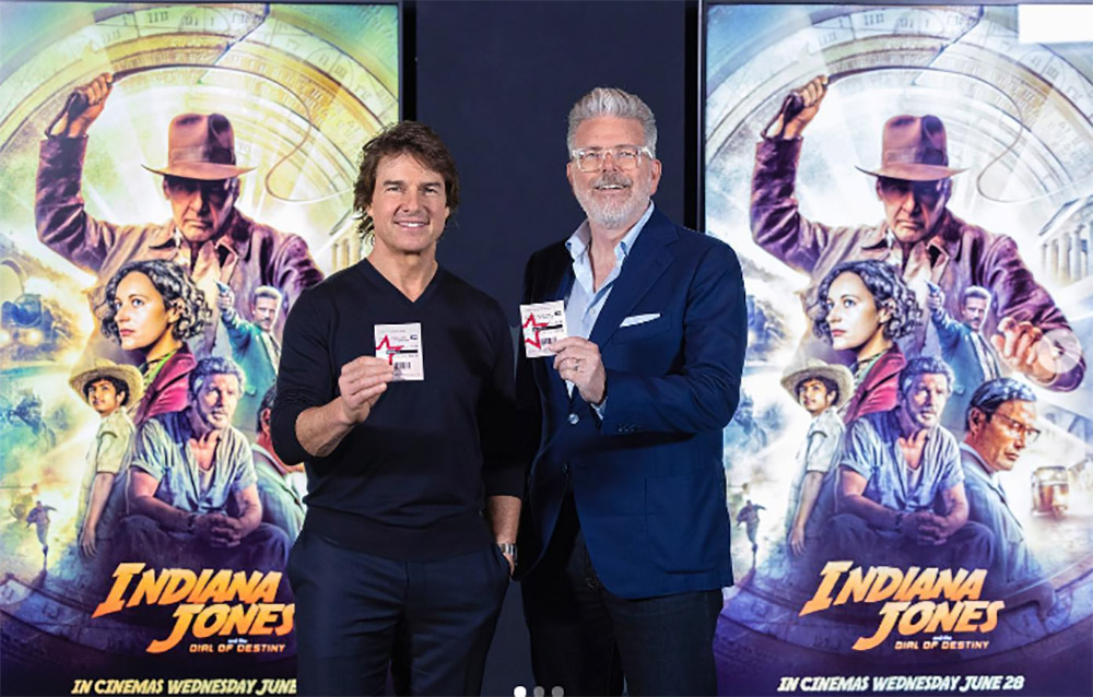 Two men holding up cinema tickets in front of Indiana Jones posters