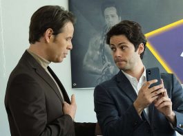 Two men in suits, one looking at the other while holding up a phone.
